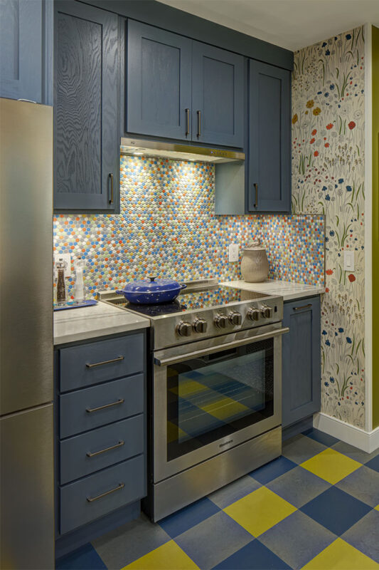 Blue kitchen cabinets with blue and yellow checkered floor and colorful backsplash.