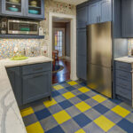 Blue kitchen cabinets with blue and yellow checkered floor and colorful backsplash.