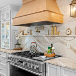 White kitchen with marble counter tops and backsplash with stained wood hood.
