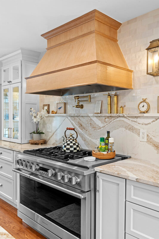 White kitchen with marble counter tops and backsplash with stained wood hood.