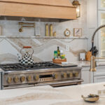 White kitchen with marble counter tops and backsplash with stained wood hood.