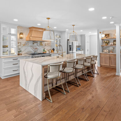 White kitchen with marble counter tops and backsplash with stained wood hood.