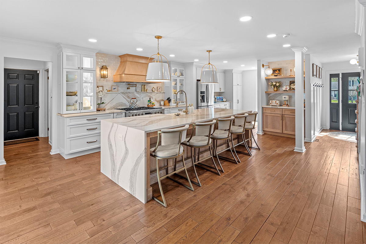 White kitchen with marble counter tops and backsplash with stained wood hood.