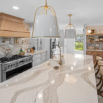 White kitchen with marble counter tops and backsplash with stained wood hood.
