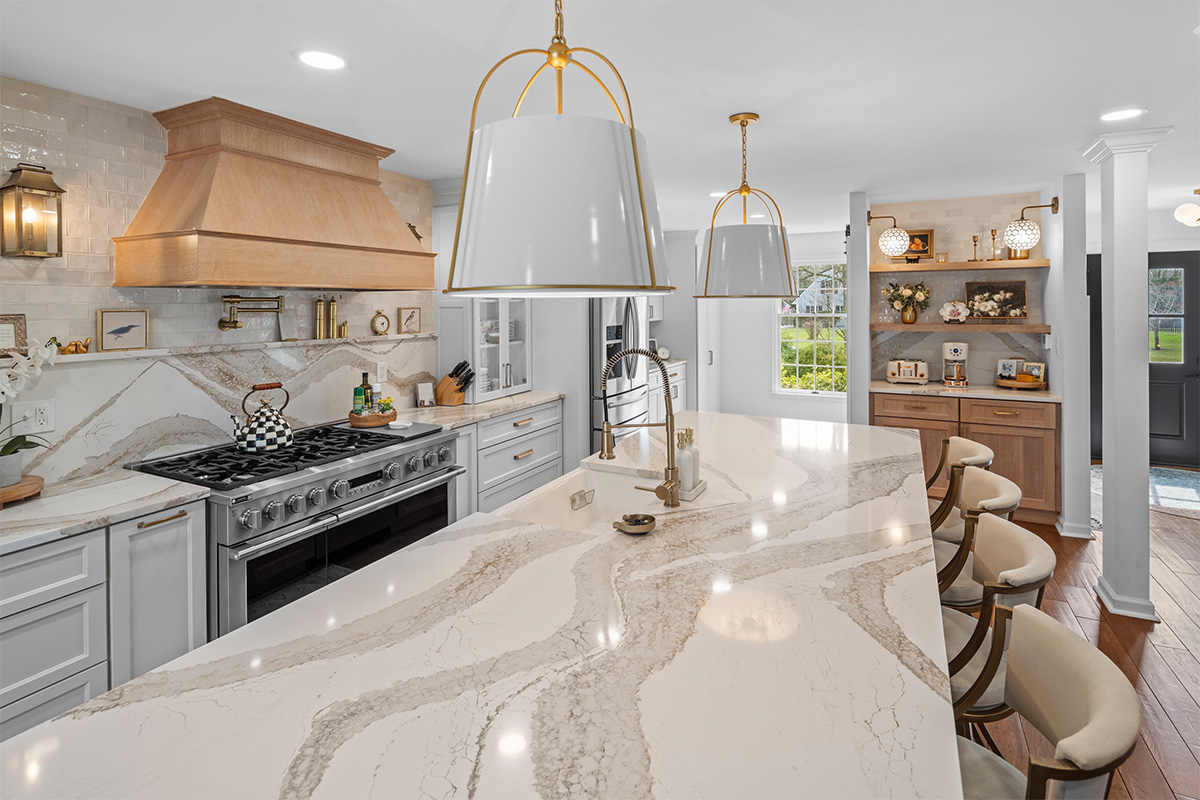 White kitchen with marble counter tops and backsplash with stained wood hood.