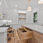 White kitchen perimeter cabinets with an island in washed out light brown Vita stain on Rift White Oak. Shows drawers open displaying organization accessories installed.