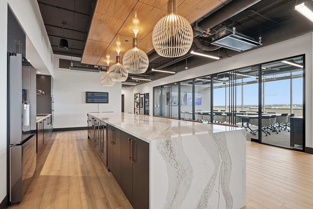 Gray painted office breakroom kitchen with long island with many seats.