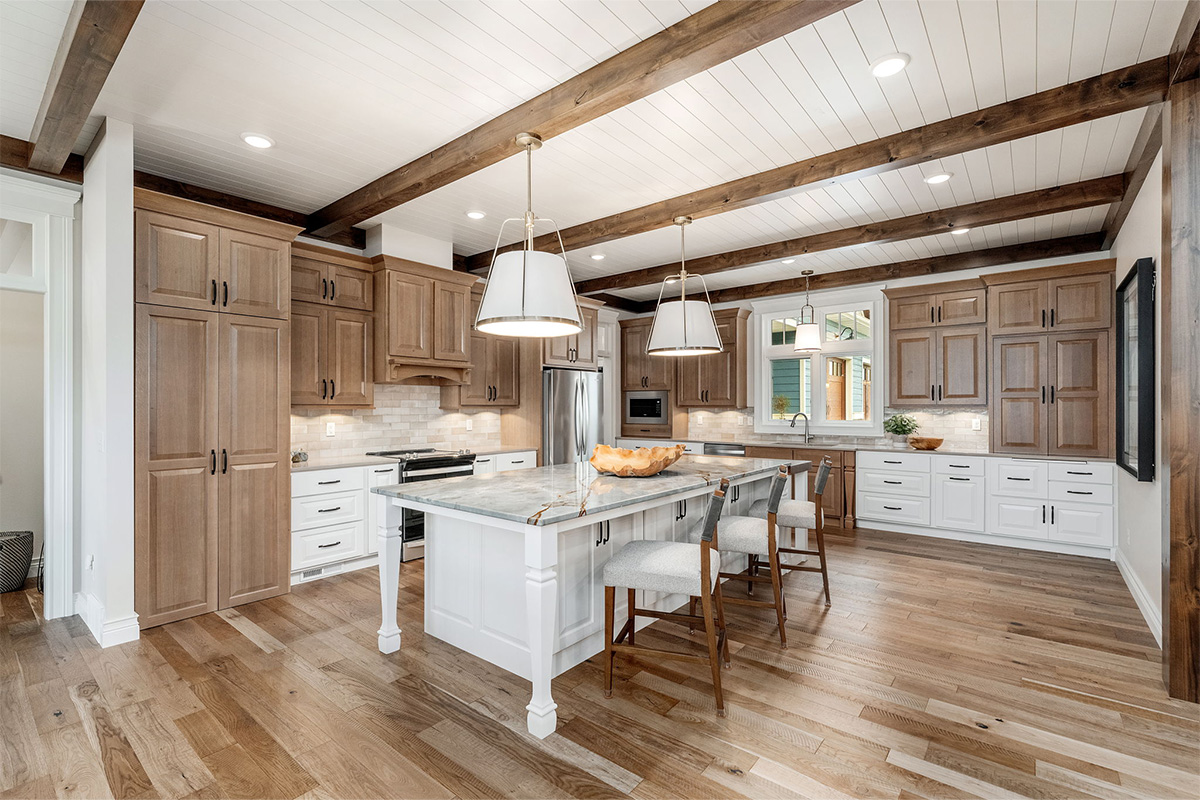 Brown-stained and white kitchen perimeter and island cabinets. Island includes decorative legs and seating.