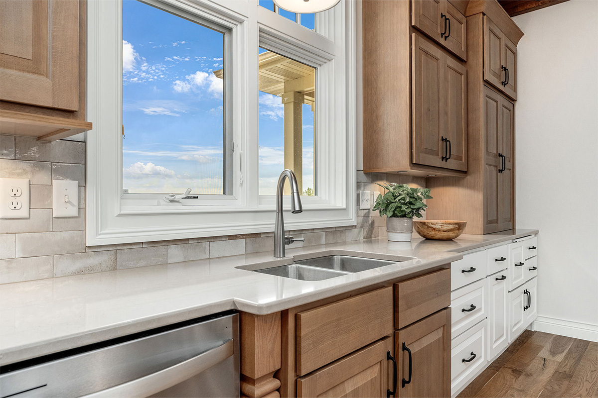 Brown-stained and white kitchen cabinets with sink by window.