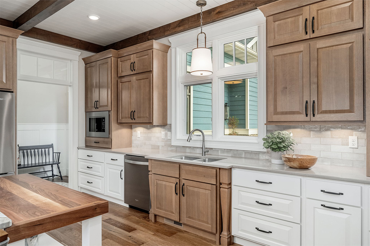 Brown-stained and white kitchen cabinets with sink by window.