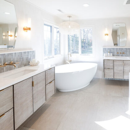 Large master bathroom with 2 vanity areas with light Montana stain, powder desk and large free-standing tub in the corner below large windows.