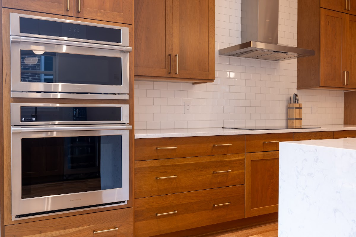 Cherry kitchen cabinets with a red Sienna stain. view shows stainless steel appliances on hood.