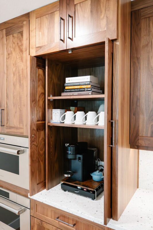 Brown-stained coffee center cabinet with open pocket doors showing coffee maker and mugs