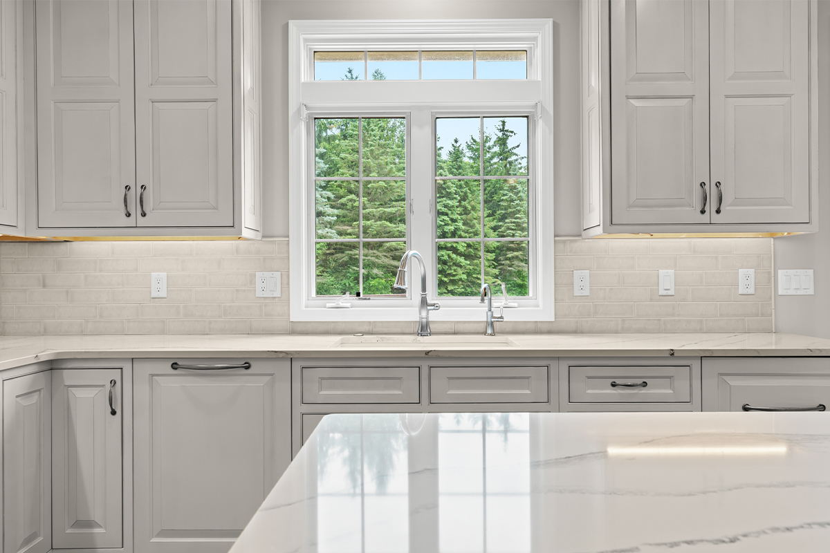 White kitchen perimeter cabinets in a view towards window above sink.