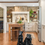 Old World style kitchen with Light Mocha-painted perimeter and a custom wood island in a mid-brown stain. 2 black labs are sitting at the front of the island.