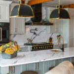 Painted Oyster primary kitchen cabinets with black appliances and green island.