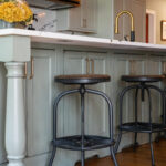 Painted Oyster primary kitchen cabinets with black appliances and green island.