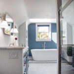 Bathroom with blue cabinetry and accent wall with white freestanding tub