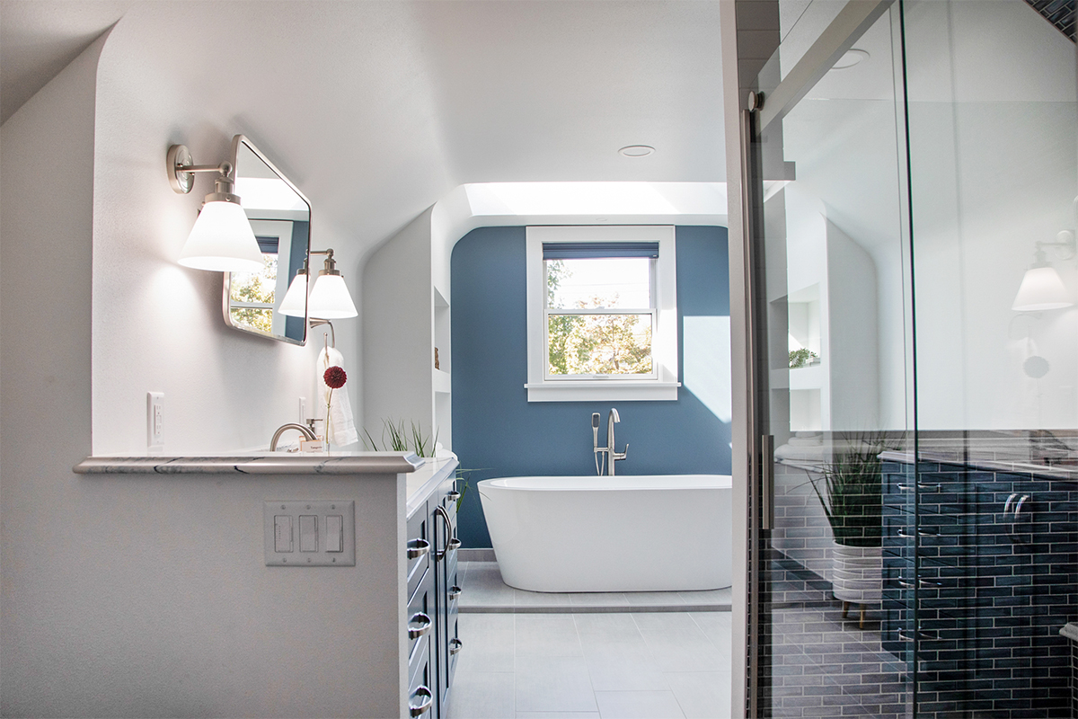 Bathroom with blue cabinetry and accent wall with white freestanding tub