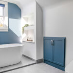 Bathroom with blue cabinetry and accent wall with white freestanding tub