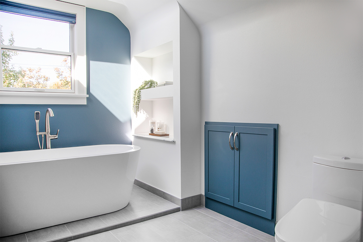 Bathroom with blue cabinetry and accent wall with white freestanding tub
