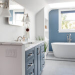 Bathroom with blue cabinetry and accent wall with white freestanding tub