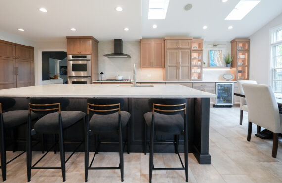 Open kitchen with perimeter cabinets in Sable stain on rift white oak and a dark island in Midnight stain.