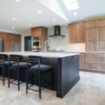 Open kitchen with perimeter cabinets in Sable stain on rift white oak and a dark island in Midnight stain.