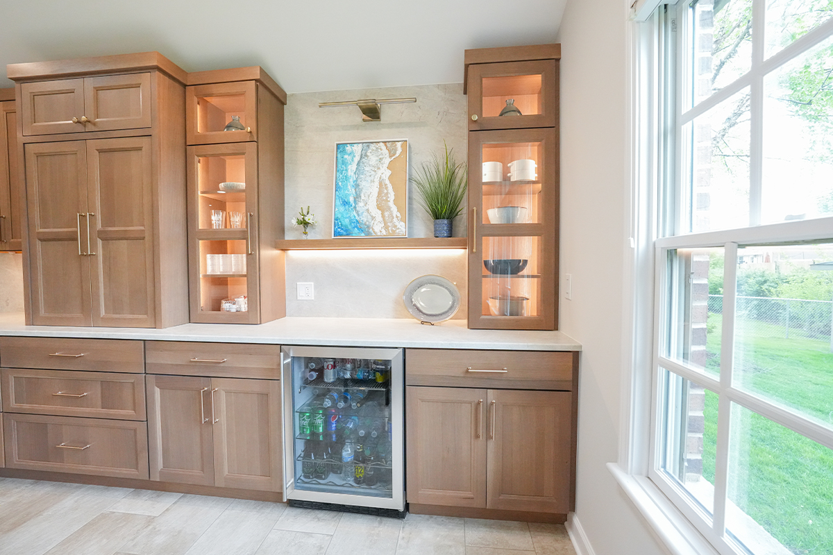 Kitchen cabinets in light brown stain with wine fridge below the counter and glass door cabinets above.