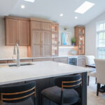 Open kitchen with perimeter cabinets in Sable stain on rift white oak and a dark island in Midnight stain.