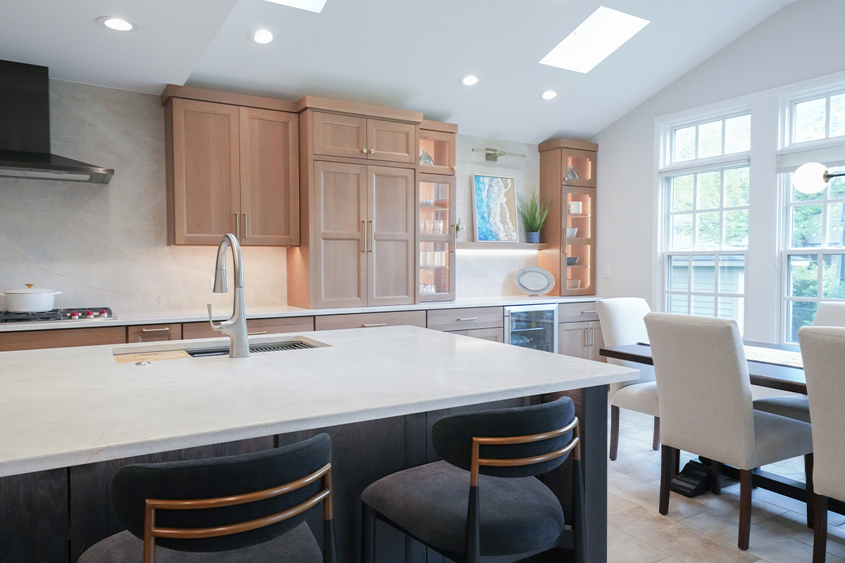 Open kitchen with perimeter cabinets in Sable stain on rift white oak and a dark island in Midnight stain.
