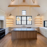 Light beige kitchen cabinets with hood and floating shelves. Also, visible is an island in rift white oak.