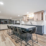 Contemporary kitchen with living room with large tv with open shelves on each side in the distance.