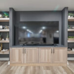 Entertainment center with large tv above light stained cabinets and open shelving on each side.