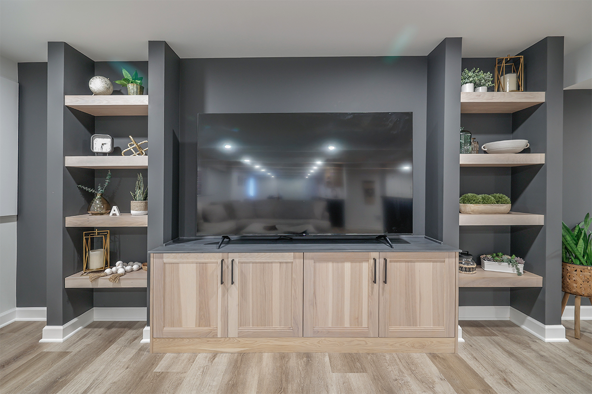 Entertainment center with large tv above light stained cabinets and open shelving on each side.