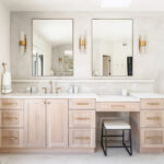 Light stained bathroom vanity with powder desk and two contemporary mirrors.