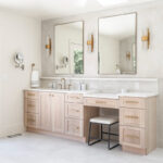 Light stained bathroom vanity with powder desk and two contemporary mirrors.