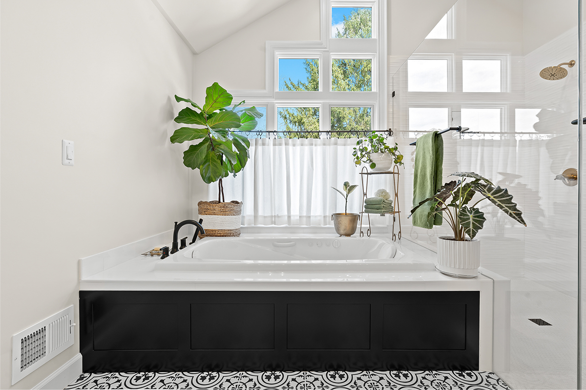 Bright and airy bathroom with several windows above the tub that has black door panel covering the front.