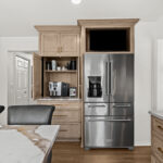 Kitchen cabinets with light brown stain and stainless steel fridge. Shows pocket doors open in a coffee center cabinet.