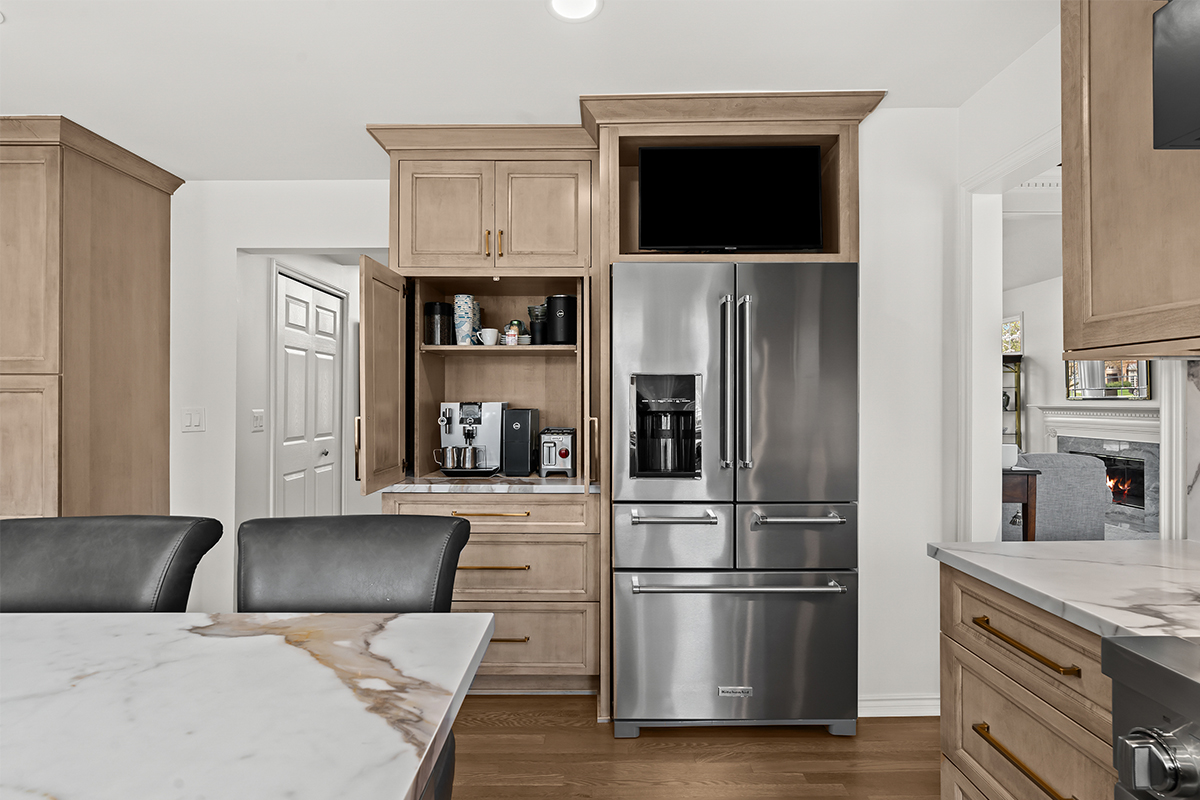 Kitchen cabinets with light brown stain and stainless steel fridge. Shows pocket doors open in a coffee center cabinet.