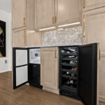 Kitchen cabinets with light brown stain and black under counter ice maker and wine fridge.