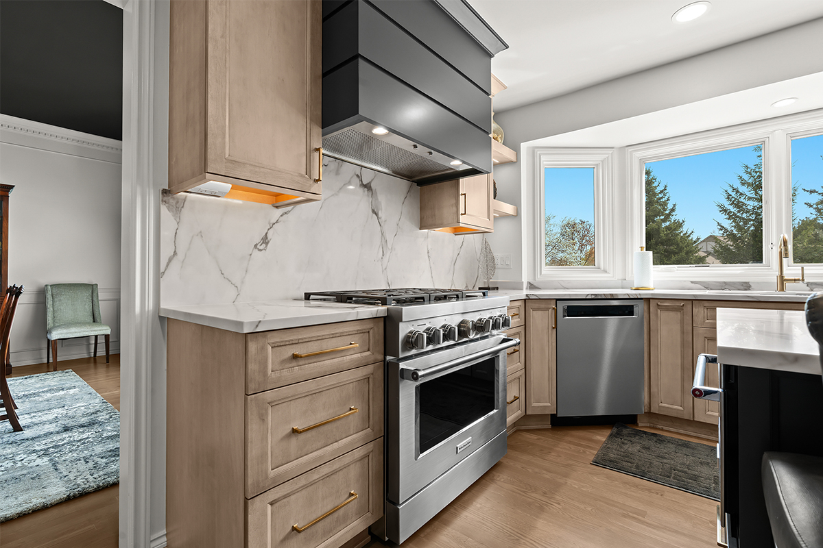 Kitchen cabinets with light brown stain. Shows a gray painted wood hood and stainless steel oven.