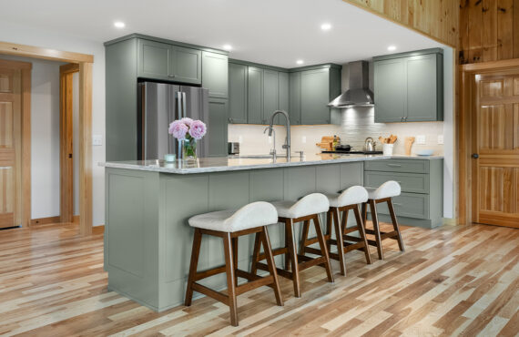 Green kitchen cabinets with island seating and light brown wood floors.