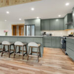 Green kitchen cabinets with island seating and light brown wood floors.