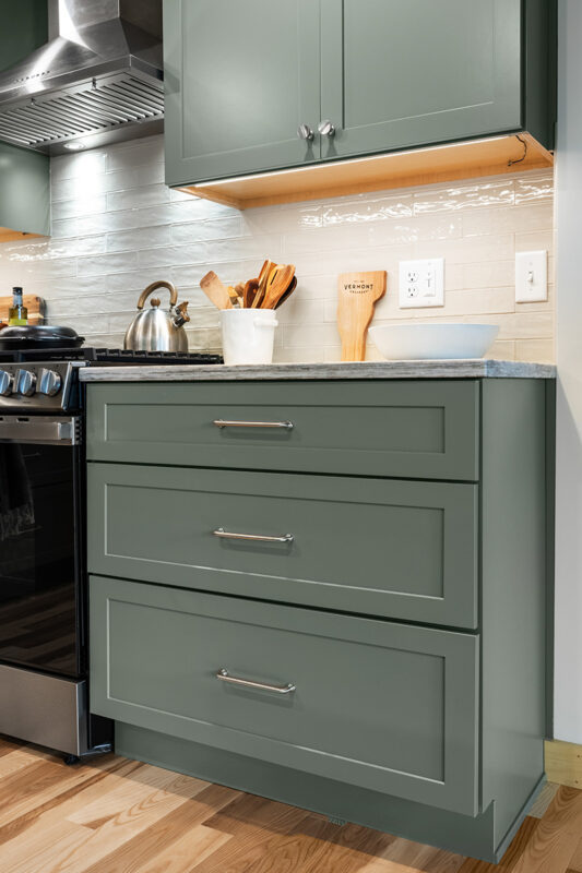 Green kitchen cabinets with island seating and light brown wood floors.