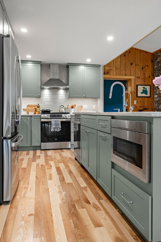 Green kitchen cabinets with island seating and light brown wood floors.