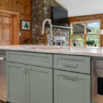 Green kitchen cabinets with island seating and light brown wood floors.