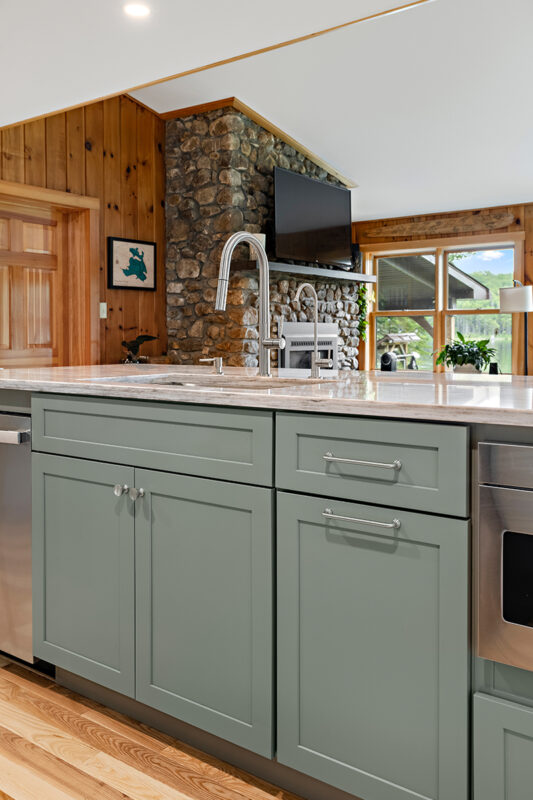 Green kitchen cabinets with island seating and light brown wood floors.