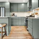 Green kitchen cabinets with island seating and light brown wood floors.
