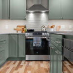 Green kitchen cabinets with island seating and light brown wood floors.